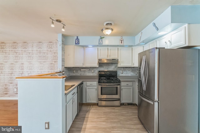 kitchen featuring visible vents, under cabinet range hood, stainless steel appliances, light wood finished floors, and decorative backsplash