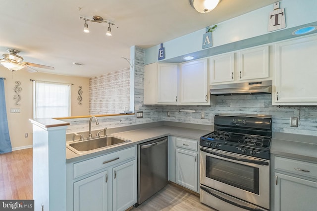 kitchen with under cabinet range hood, decorative backsplash, appliances with stainless steel finishes, a peninsula, and a sink