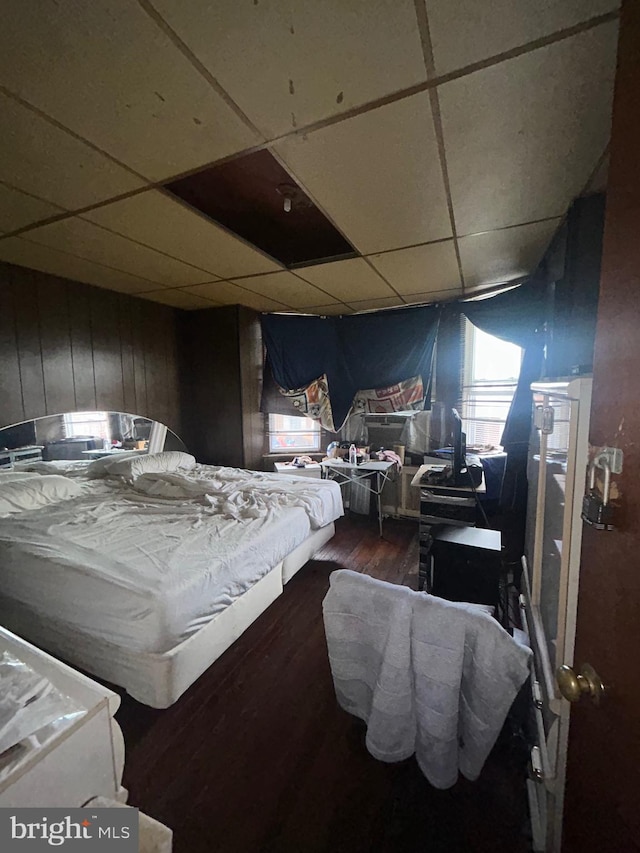 bedroom with hardwood / wood-style flooring, a drop ceiling, and wooden walls