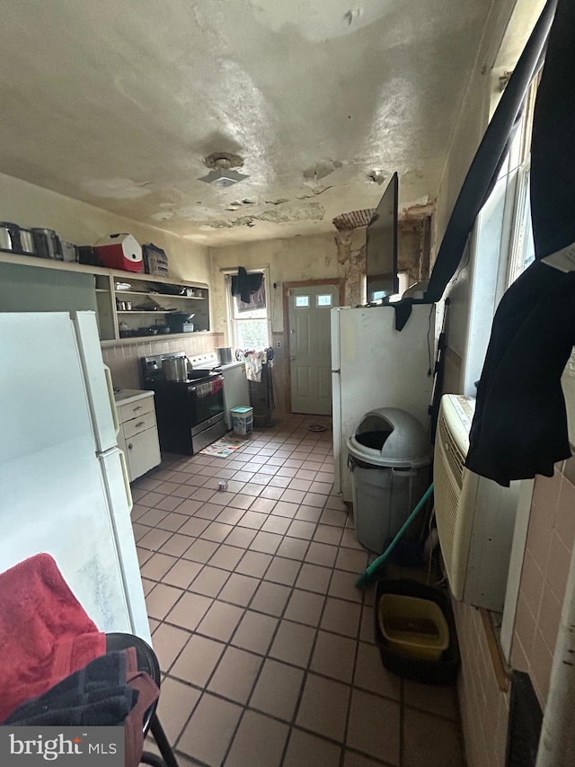 interior space with black / electric stove, white cabinetry, light tile patterned floors, and white refrigerator