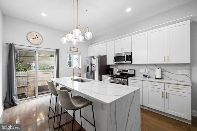 kitchen featuring a center island with sink, a sink, white cabinetry, stainless steel appliances, and decorative backsplash