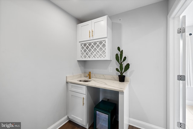 bar featuring light stone countertops, dark hardwood / wood-style flooring, white cabinetry, and sink