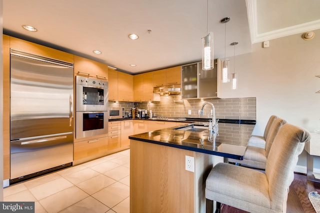 kitchen featuring a peninsula, a sink, light brown cabinetry, stainless steel appliances, and dark countertops