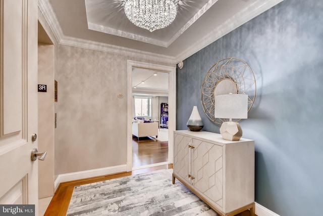 corridor with light wood-type flooring, a tray ceiling, and crown molding