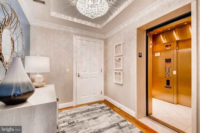 foyer with light wood-type flooring, a tray ceiling, ornamental molding, and elevator