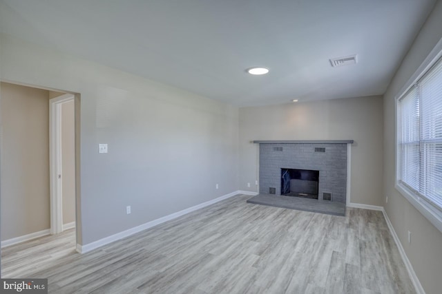 unfurnished living room featuring a brick fireplace and light hardwood / wood-style floors