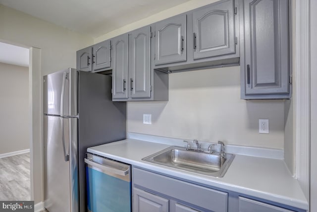 kitchen with light wood-type flooring, gray cabinets, stainless steel appliances, and sink