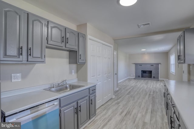 kitchen with a fireplace, light wood-type flooring, dishwasher, sink, and gray cabinetry