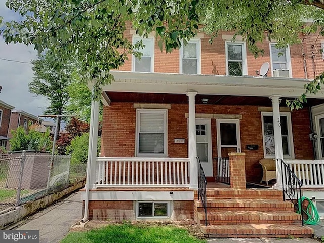 view of front of property featuring a porch, fence, and brick siding