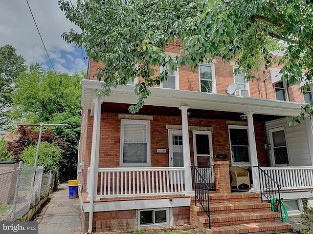 multi unit property featuring brick siding, a porch, and fence