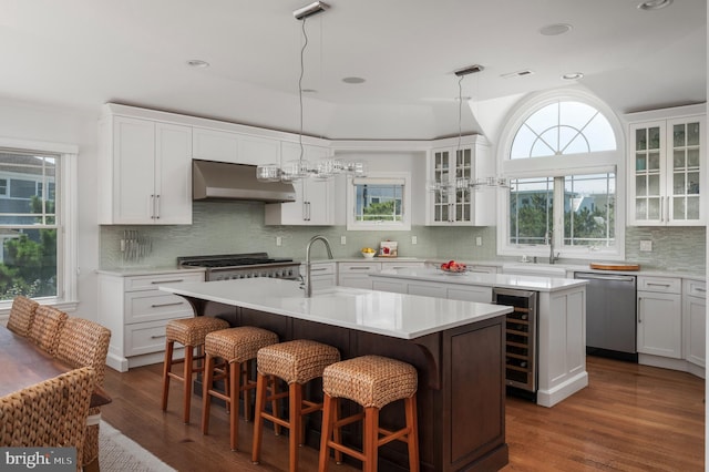 kitchen featuring a center island with sink, appliances with stainless steel finishes, a sink, ventilation hood, and beverage cooler