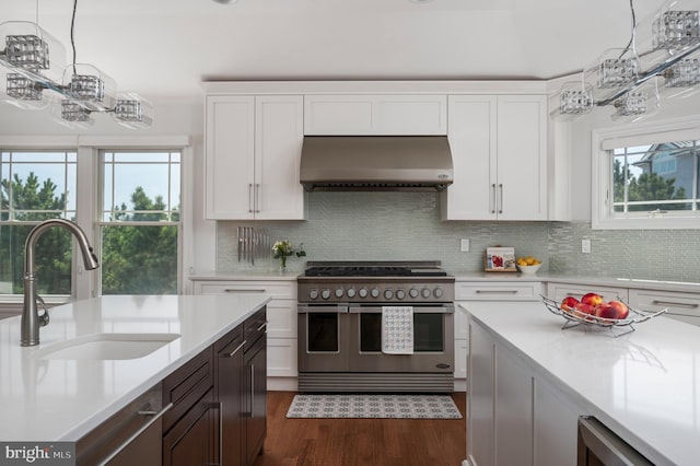 kitchen featuring wall chimney exhaust hood, range with two ovens, a sink, and light countertops