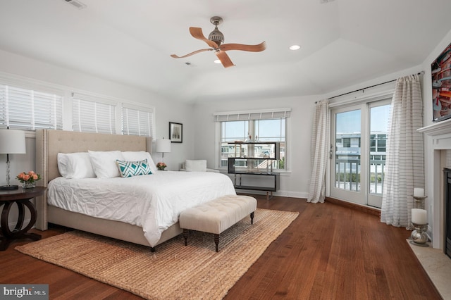 bedroom with a fireplace with flush hearth, a raised ceiling, multiple windows, and wood finished floors