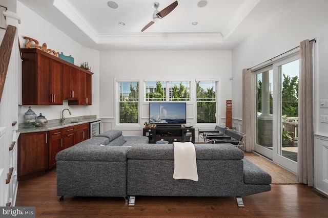 living room with wainscoting, dark wood-style floors, ceiling fan, wine cooler, and a tray ceiling