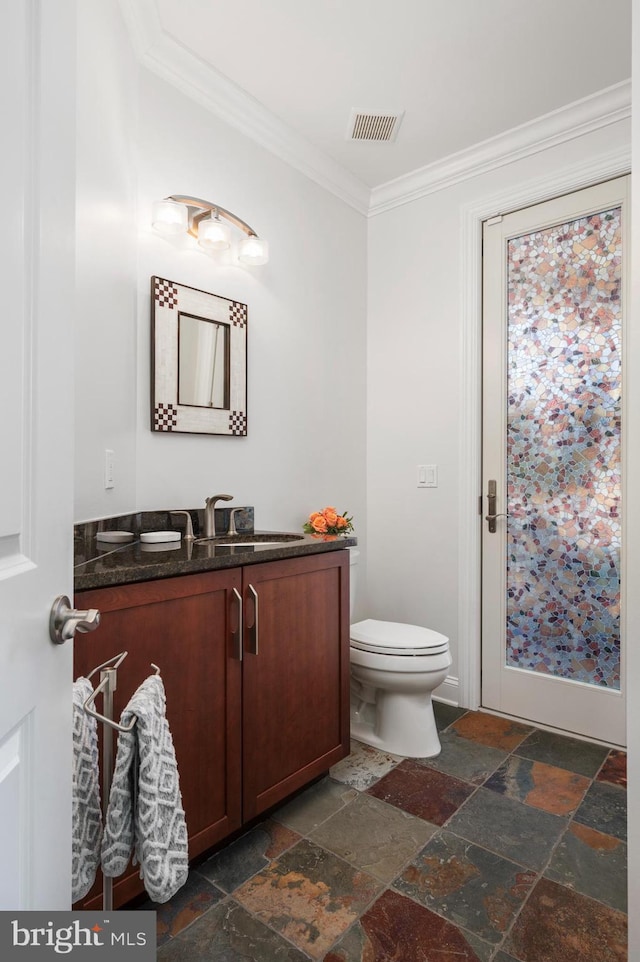 half bathroom featuring toilet, visible vents, vanity, stone tile flooring, and crown molding