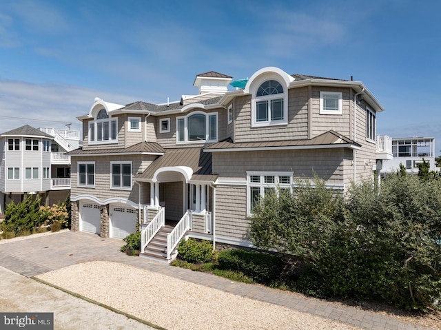 shingle-style home with decorative driveway, a standing seam roof, metal roof, and a garage