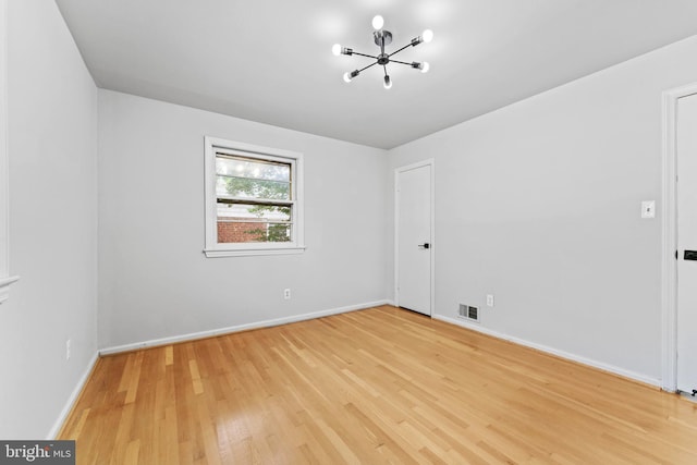 spare room with an inviting chandelier and light wood-type flooring