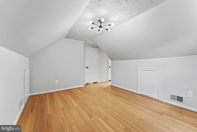 additional living space with an inviting chandelier, vaulted ceiling, a textured ceiling, and light hardwood / wood-style floors