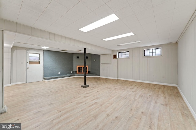 basement with light wood-type flooring, wooden walls, a wood stove, and brick wall