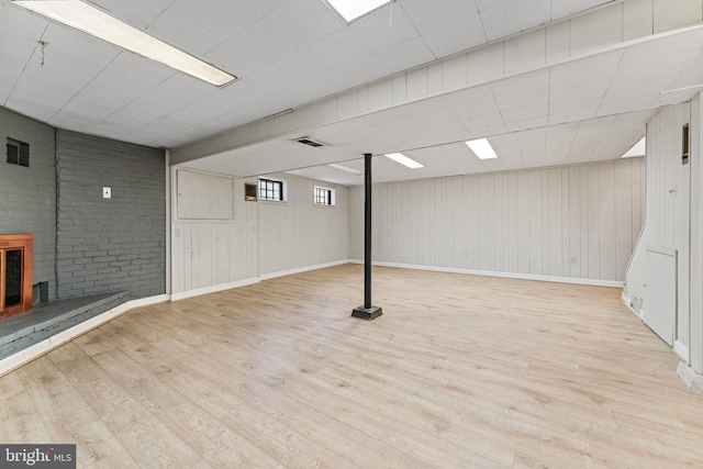 basement featuring brick wall, wooden walls, and light wood-type flooring