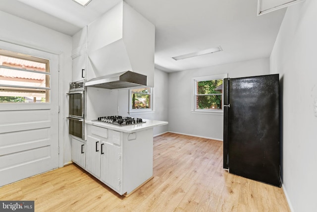 kitchen with light hardwood / wood-style flooring, stainless steel appliances, white cabinetry, and wall chimney range hood