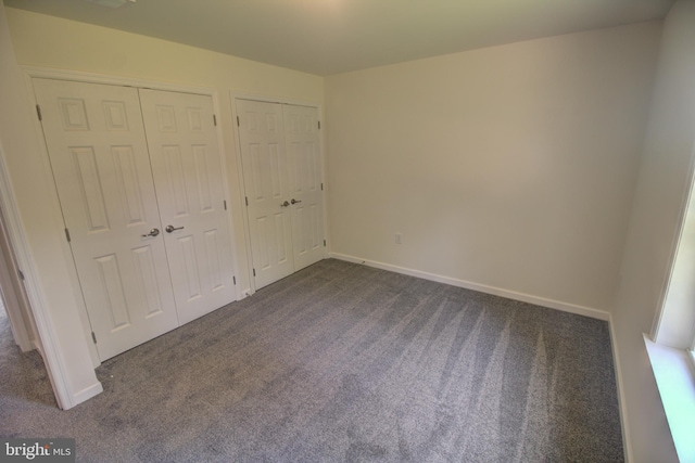 unfurnished bedroom featuring two closets and dark colored carpet