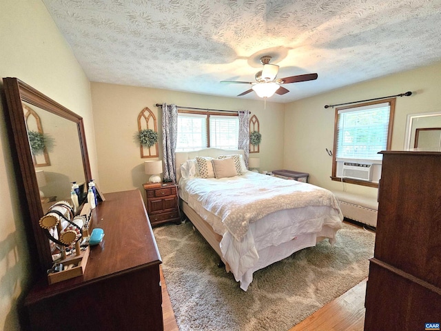 bedroom featuring a textured ceiling, baseboard heating, cooling unit, ceiling fan, and hardwood / wood-style flooring