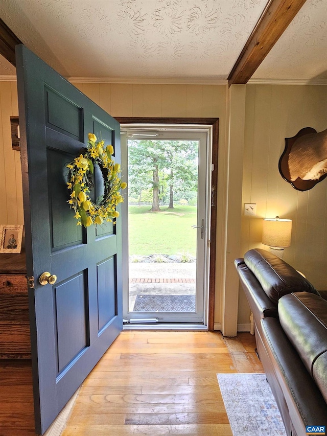 doorway with a textured ceiling, beamed ceiling, and light wood-type flooring