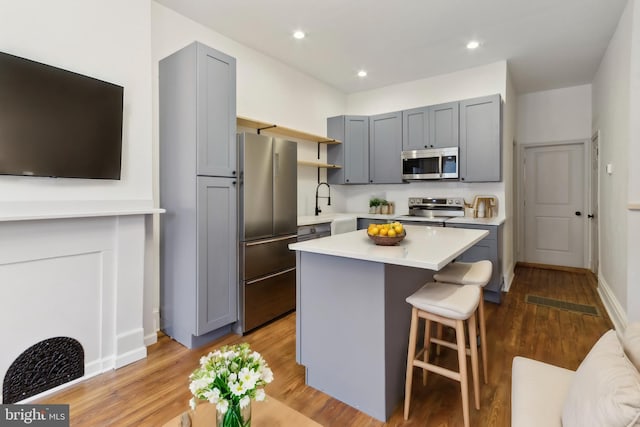 kitchen with gray cabinets, appliances with stainless steel finishes, light hardwood / wood-style flooring, and a kitchen island