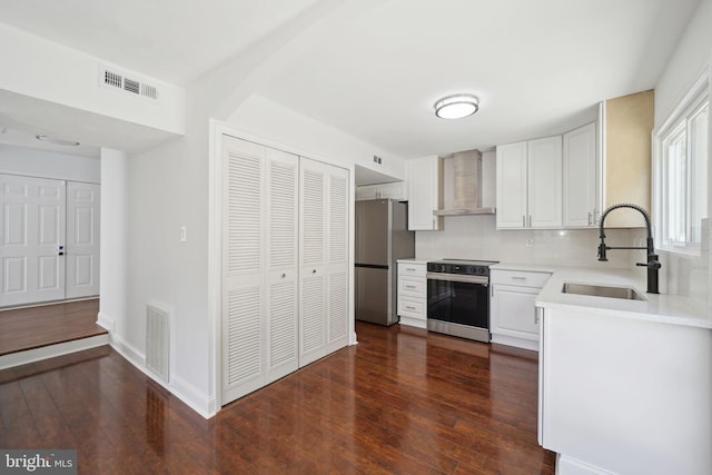 kitchen with sink, white cabinets, decorative backsplash, stainless steel appliances, and wall chimney range hood