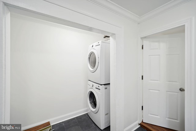 laundry area featuring stacked washer and dryer, ornamental molding, and dark tile patterned floors