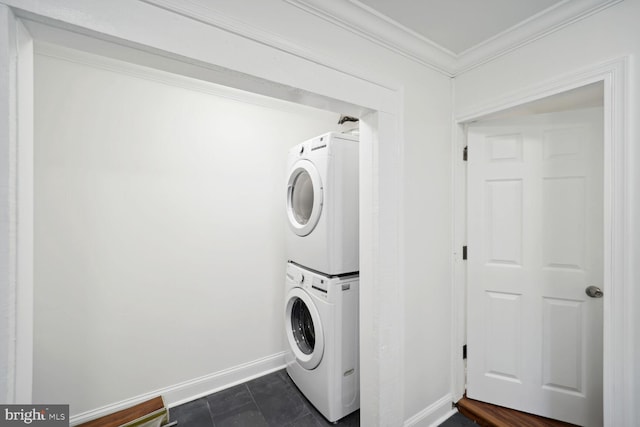 laundry room with crown molding, stacked washer / drying machine, and dark tile patterned flooring