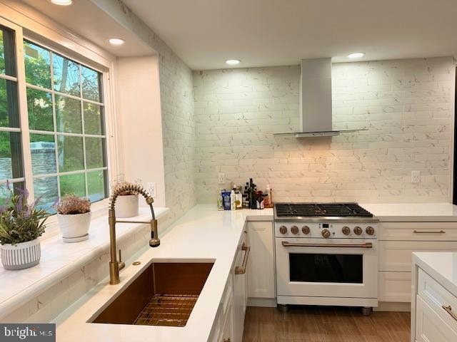 kitchen with white cabinets, hardwood / wood-style flooring, range with gas cooktop, sink, and wall chimney exhaust hood