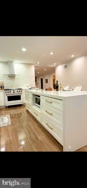 interior space with range with gas stovetop, wall chimney exhaust hood, tasteful backsplash, and light hardwood / wood-style flooring