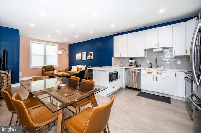 kitchen with white cabinets, tasteful backsplash, appliances with stainless steel finishes, light wood-type flooring, and sink