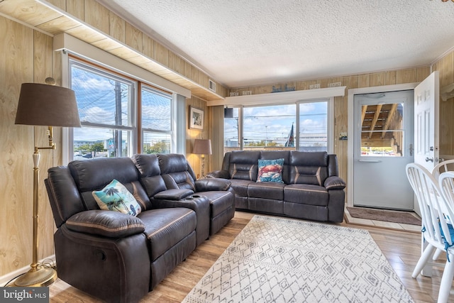 living room featuring plenty of natural light, light wood-style floors, wood walls, and a textured ceiling