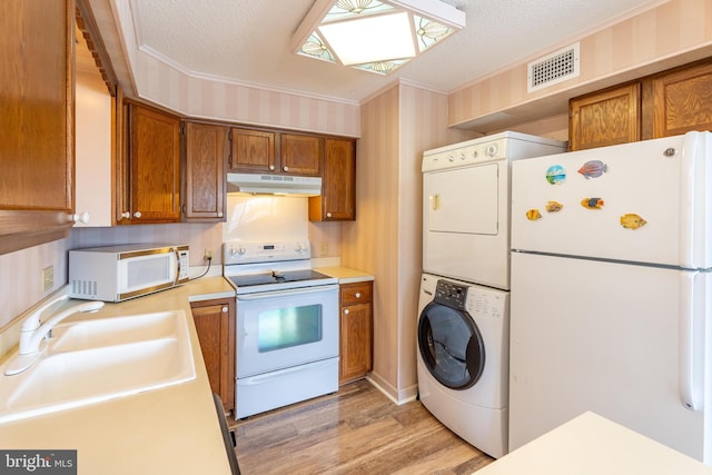 kitchen featuring visible vents, stacked washer and dryer, under cabinet range hood, a sink, and white appliances