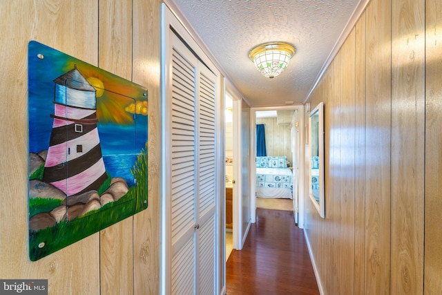 hall featuring a textured ceiling, wood finished floors, and wooden walls