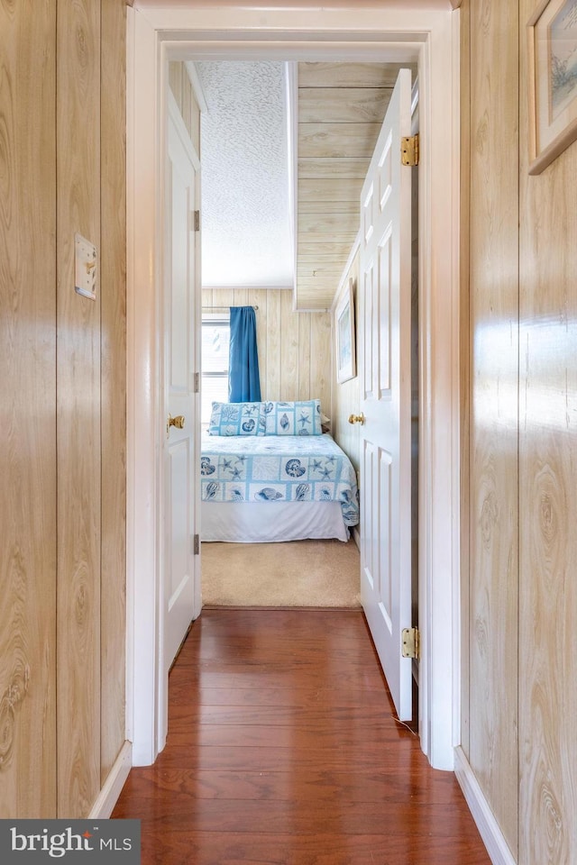 corridor featuring wooden walls, a textured ceiling, and wood finished floors