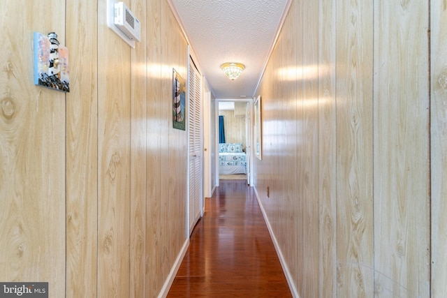 hall featuring a textured ceiling, dark wood-type flooring, and wooden walls