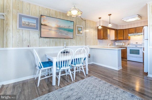 kitchen featuring white appliances, brown cabinetry, dark wood-style floors, a peninsula, and under cabinet range hood