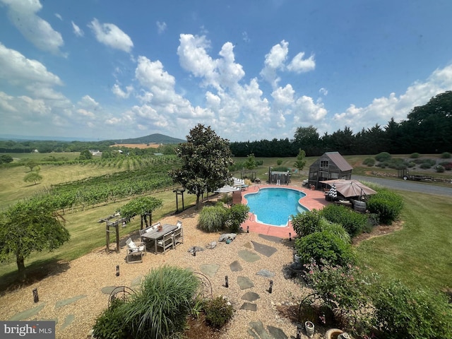 outdoor pool with a patio, a rural view, fence, and an outbuilding