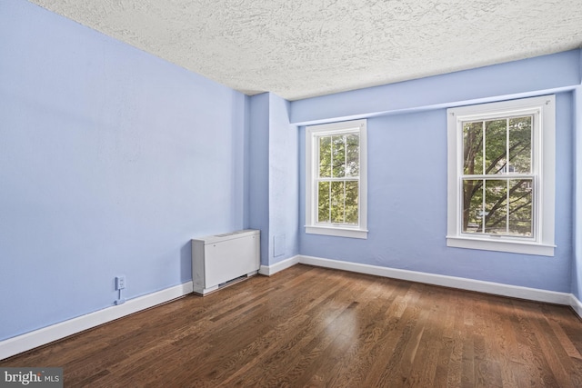 empty room featuring a textured ceiling, dark hardwood / wood-style floors, and plenty of natural light