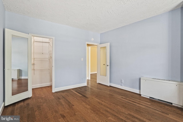 unfurnished bedroom with a spacious closet, a closet, dark hardwood / wood-style floors, and a textured ceiling