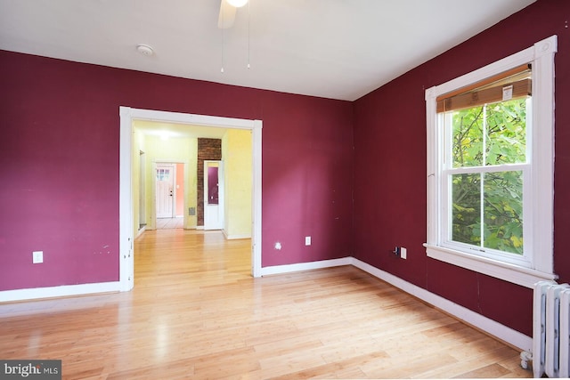 unfurnished room featuring light wood-type flooring, ceiling fan, and radiator heating unit