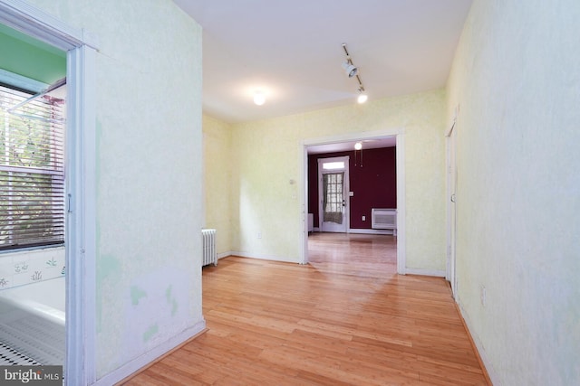 hall featuring radiator, light hardwood / wood-style flooring, a wall unit AC, and track lighting