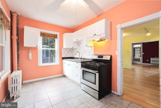 kitchen with light hardwood / wood-style floors, white cabinets, radiator, ceiling fan, and gas stove