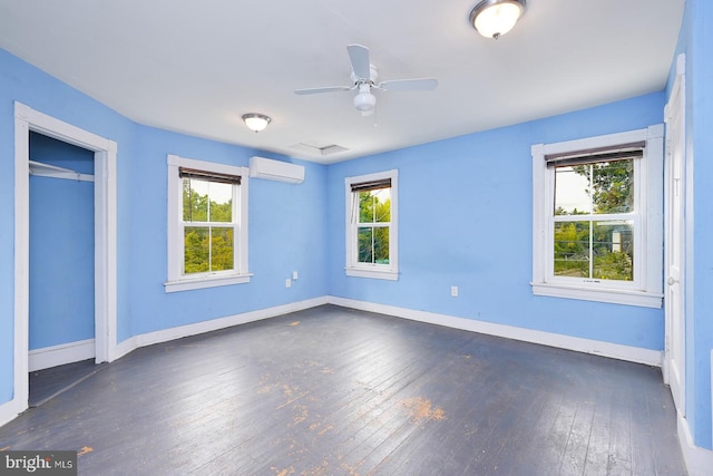 unfurnished bedroom featuring a wall unit AC, multiple windows, and dark hardwood / wood-style floors