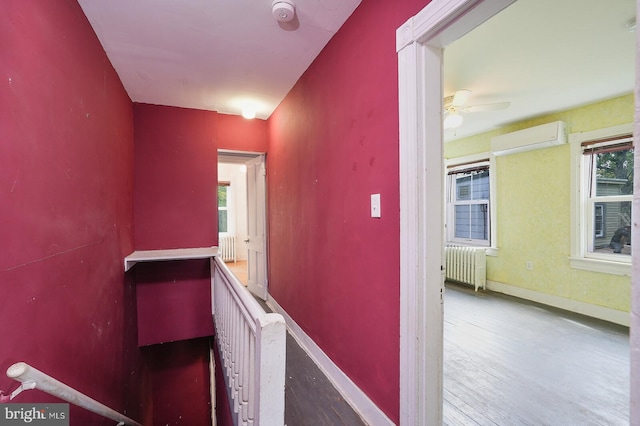 hallway featuring hardwood / wood-style flooring, a wall mounted air conditioner, and radiator heating unit