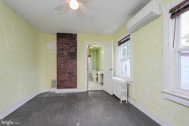 unfurnished room featuring radiator, dark wood-type flooring, a wall mounted air conditioner, and a wealth of natural light